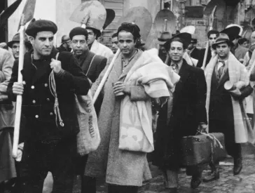 Black and white photograph: a group of men with shovels walking along a street.
