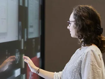Several people stand in front of a digital wall on which documents and photos are displayed. One of the people touches the media installation to interact with it.