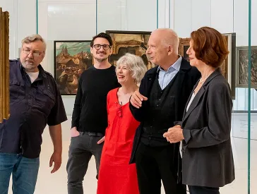 Besucher*innen einer Kunstausstellung betrachten Gemälde.