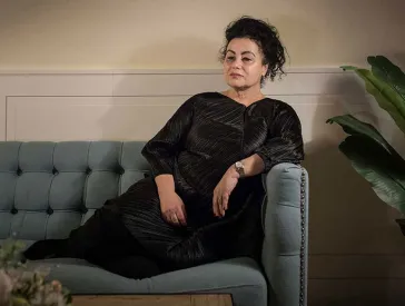 Woman in black dress sits on a sofa.