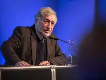 Portrait of Micha Brumlik at the podium speaking into a microphone