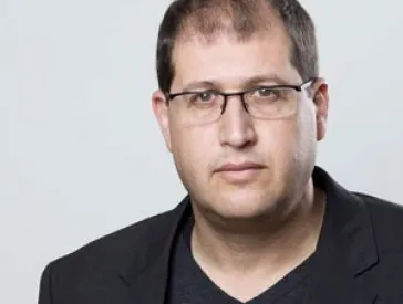 Portrait of a man in a black suit with glasses.