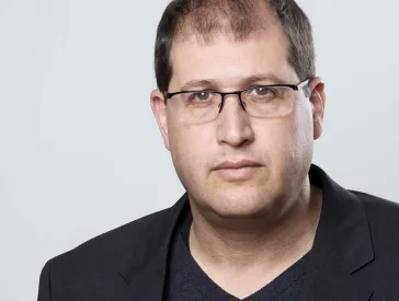 Portrait of a man in a black suit with glasses.