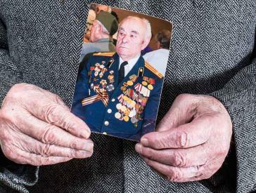 Hands holding a photo of a man wearing a uniform adorned with many ribbons and medals.
