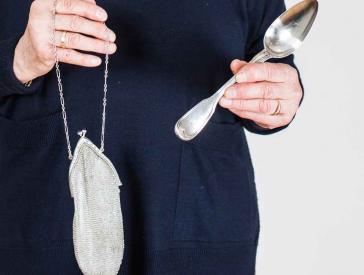 Elderly lady holding a silver bag and a silver spoon in her hands.