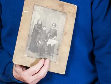 Ein älteres Ehepaar hält eine alte Schwarz-Weiß-Fotografie in Händen.