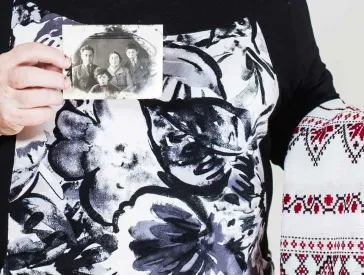 Ein ältere Dame hält ein besticktes Hochzeitstuch und eine Schwarz-Weiß-Fotografie in Händen.