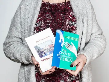 Zwei Hände mit dunkelrotem Nagellack halten zwei Bücher.