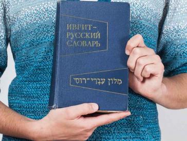 Hände halten ein Buch mit hebräischer und kyrillischer Schrift.