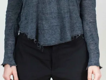 Bildausschnitt eines Körpers mit grauem Pullover, schwarzer Hose und Händen.