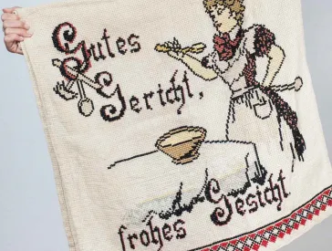 Eine junge Frau mit langem Haar hält einen bestickten Wandteppich in Händen.