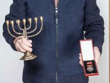 Ein Mann hält eine Menora in der einen und einen Orden in der anderen Hand.