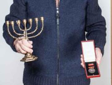 A man holds a menorah in one hand and a medal in the other.