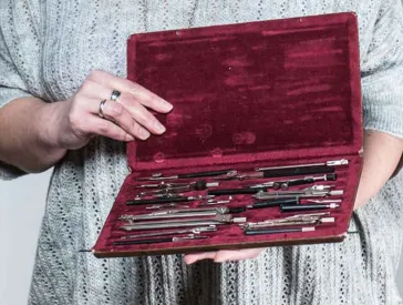 Eine Frau hält einen samtgefütterten geöffneten Kasten mit Zeichenmaterial in der Hand.
