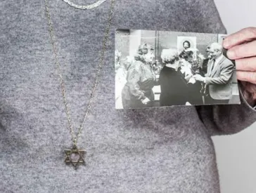 Eine Frau stützt sich auf einen Gehstock und hält zwei Fotos in der Hand.