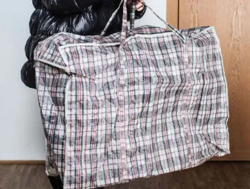 Eine Frau in dicker Winterjacke trägt riesige karierte Platiktasche.