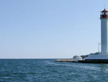 View of the sea, a lighthouse on the right, tall houses in the background.