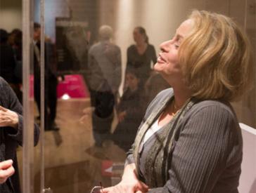 A woman stands at the opening of a showcase and talks to a crowd of visitors.