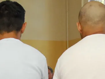 Zwei Männer sitzen auf einem roten Würfel, ihre Rücken und Hinterköpfe sind der Kamera zugewandt.