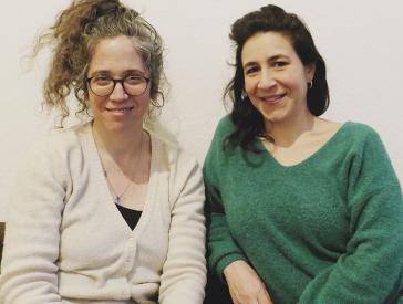 Two women sit next to each other and smile at the camera.
