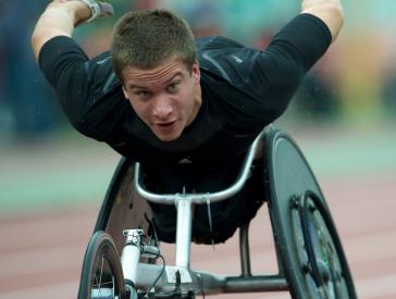 A racing wheelchair rider in a black jersey rides on a racetrack.