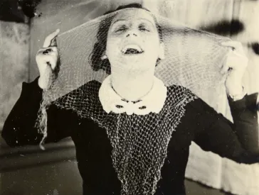 Porträt einer Frau, die sich Spitzenstoff vor ihr Gesicht hält