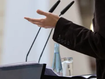 A person stands in front of a lectern with microphones.