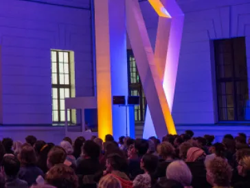 The glass courtyard is filled with people and illuminated in purple.