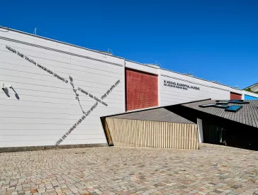 Blick von der Seite auf den h&ouml;lzernen Haupteingang des Akademiegeb&auml;udes.