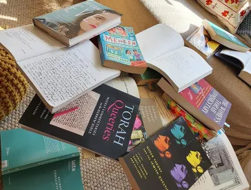 Messy stack of books with titles such as Torah Queeries, Becoming Eve, Queer Theory and the Jewish Question, and Mentsh