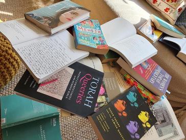 Messy stack of books with titles such as Torah Queeries, Becoming Eve, Queer Theory and the Jewish Question, and Mentsh