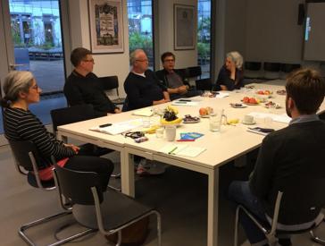 Six people sit around a table and talk.