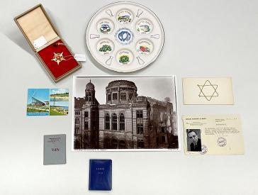 Ein goldener fünfzackiger Stern mit Hammer und Sichel, ein Seder-Teller, eine Postkarte aus Glowe, ein Foto der zerstörten Synagoge in der Oranienburgerstraße und verschiedene Ausweise