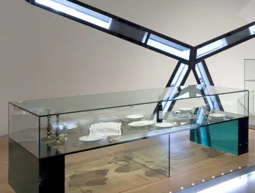 In einer Glasvitrine sind Teller, Weinflaschen und Kerzenständer ausgestellt.