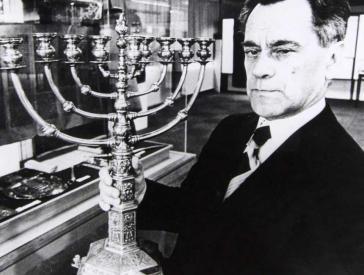 Black and white photograph of a man with hanukkah candlestick in his hand.