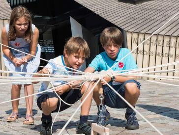 Three children are playing at a game of knots.