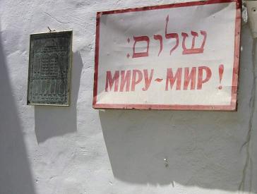 Hauswand mit einem Schild, auf dem in hebräischen Buchstaben Shalom und auf Russisch Friede für die Welt steht