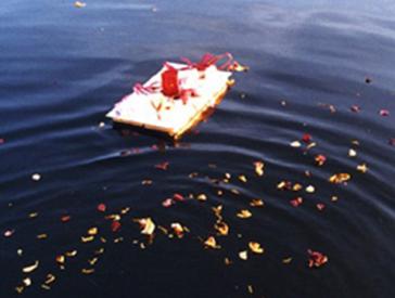 Blüten und Papierschiff treiben im Wasser.