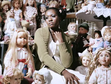 Eine junge Frau sitzt in einem Raum gefüllt mit Puppen.