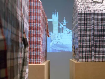 Aus rot-weiß- und blau-weiß-karierten Plastikreisetaschen gemachte Häuser auf Pappkartons