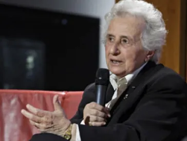 Older lady with microphone in armchair, talking.