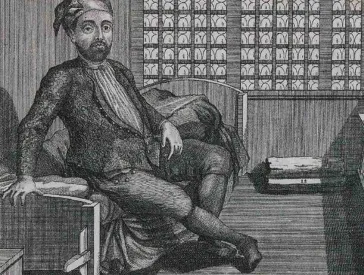 A man with a blank stare sits on a bed in a cell.