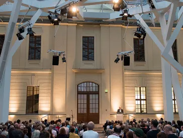 Visitors in the glass courtyard of the Jewish Museum Berlin listening to an event.