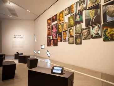 An den W&auml;nden h&auml;ngen bunt bemalte Portr&auml;ts von M&auml;nnern und Frauen vor schwarzen St&uuml;hlen mit Tablets.