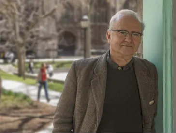 Mann steht seitlich angelehnt an einer Wand, im Hintergrund Menschen und B&auml;ume