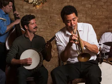 Three male members of a jazz combo play their insturments in front of a brick wall.