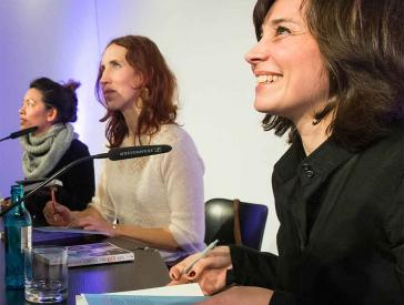 Three women in profile at a table, smilingly signing books