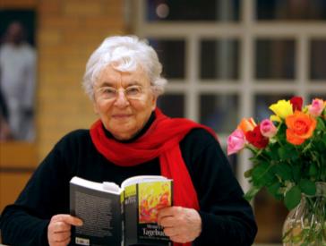 Woman with open book in hands looks friendly into camera.