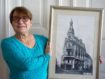 Eine Frauen hält ein Bild mit einer Gebäudeansicht in die Kamera.