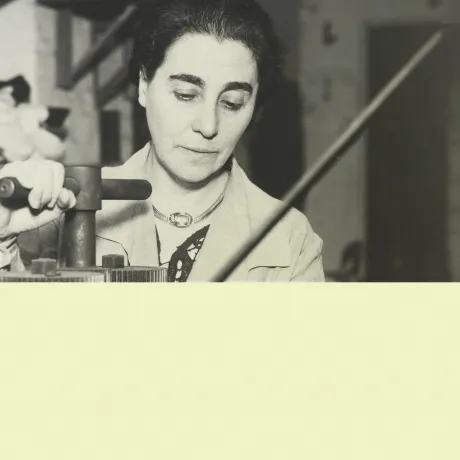 A black and white photo features a woman standing at a press.